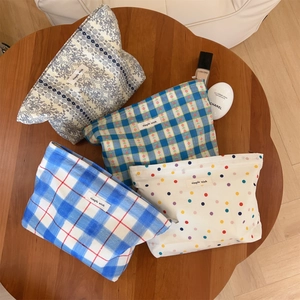 Flat lay of four floral and plaid canvas makeup bags with zippers on a wooden table