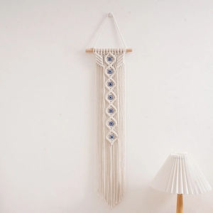 Detail of woven cotton macrame wall hanging featuring blue evil eye beads and tassels