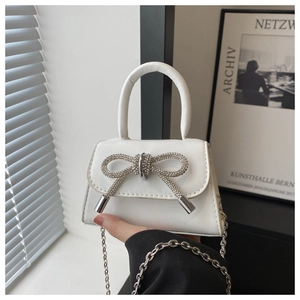 Detail of white mini handbag featuring a sparkling silver rhinestone bow and metal chain