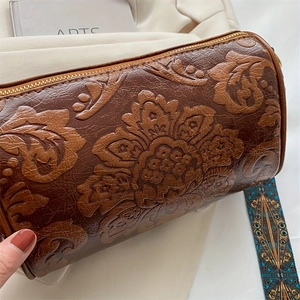 Close-up of vintage floral embossed leather texture and gold zipper on a cylinder bag