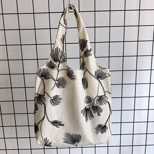 Close-up of beige canvas tote bag featuring black floral embroidery on a metal grid background