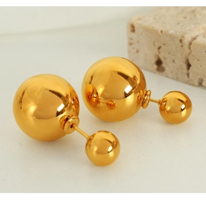 Macro shot of polished gold titanium steel double ball earrings on a textured stone