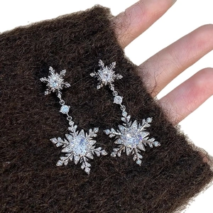 Sparkling silver snowflake pendant earrings with clear zircon stones on brown fabric