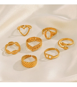 Detail view of seven golden stainless steel rings with heart and snake designs on silk