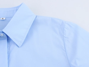 Detailaufnahme eines hellblauen Popeline-Hemdkragens mit Perlenknopf und feinen Nähten