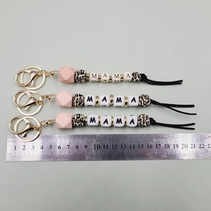 Detail view of MAMA silicone bead keychains with tassel and metal ruler for size scale