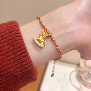 Détail d'un charm de cheval à bascule plaqué or 24K sur un bracelet tressé rouge au poignet