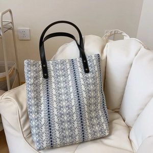 Floral cotton tote bag with blue lace patterns and black leather handles on white sofa