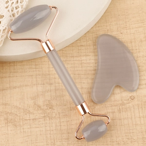 Close-up of grey resin facial roller and heart-shaped gua sha tool set on a wooden base