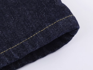 Détail macro d'un poignet en jean bleu foncé avec doubles coutures jaunes renforcées
