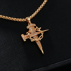 Macro shot of gold cross pendant with nail design, zircon stones and snake detail on box chain