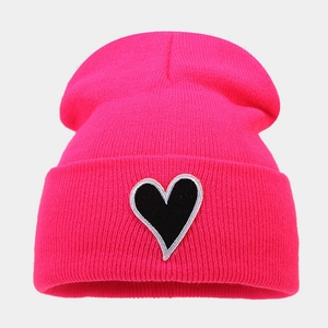 Close-up of rose red knit beanie showing heart patch detail and ribbed texture
