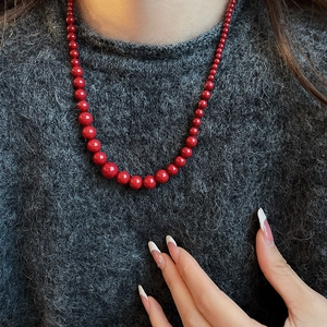 Collier de perles rouge foncé porté sur un pull gris foncé pour un look automne élégant