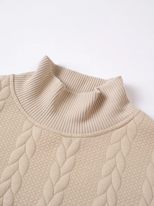 Close-up of beige knit sweater showing detailed cable weave and ribbed turtle neckline