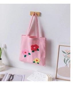 Detail of pink canvas tote bag with 3D floral embroidery hanging on a wall hook