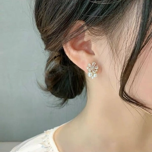 Detail of flower stud earring with zircon stones and pearl on model's ear