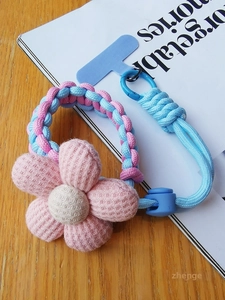 Close-up of woven phone lanyard with pink plush sponge flower and blue clip on wooden desk