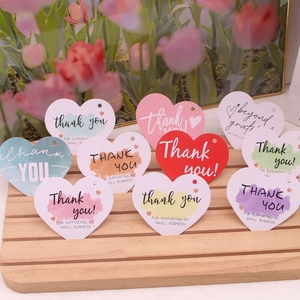 Assorted colorful heart-shaped thank you gift tags displayed on a rustic wooden stand