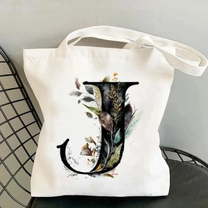 Detail of white canvas tote bag featuring floral letter J design on a black iron chair