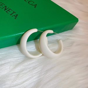 Detailed macro shot of white resin C-shaped hoop earrings with silver pins on soft plush