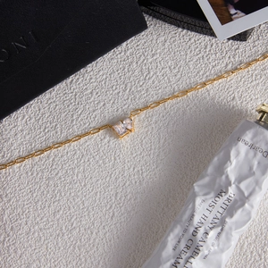 Detail of golden titanium steel necklace with two square zircon pendants on white surface