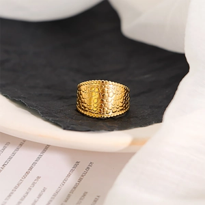 Close-up of gold-plated wide band ring with crocodile scale texture and beaded edges