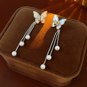 Detalle de pendientes de mariposa con perlas y borlas de flecos plateados finos
