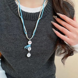 Détail du pendentif bonhomme de neige avec écharpe bleue sur pull gris foncé