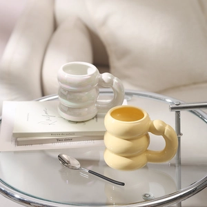 Detailed view of bubble ceramic mugs in pearl white and soft yellow on a glass table