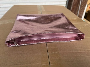 Close-up of pink metallic PU leather makeup bag with silver zipper on a box surface