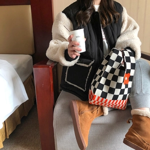 Knitted tote bag with checkered pattern and flower charm held by a model in casual outfit