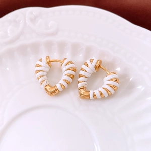 Detail of 18k gold heart hoop earrings with white thread wrapping on ceramic plate