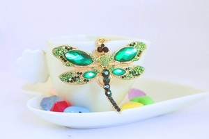 Macro detail of a dragonfly keychain with green rhinestones in a white ceramic cup