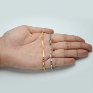 Detailed close-up of gold and silver box chain bracelets held in palm on gray background