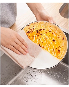 Luffa dishcloth cleaning orange sauce stain from a white ceramic plate in kitchen