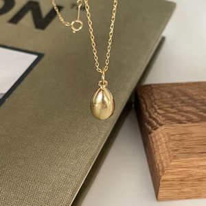 Polished gold teardrop pendant on thin chain resting on dark green book and wood