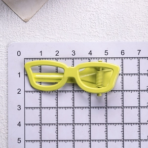 Sunglasses shaped hair clip in neon yellow metal on a measurement scale background