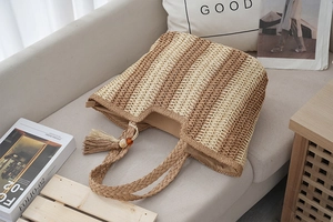 Close-up of striped straw tote bag featuring decorative fringe tassel and woven handles