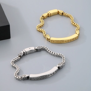 Detail of silver and gold stainless steel curb bracelets with Greek fret engraved plates