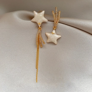 Detail of asymmetric gold tassel earrings with zircon stars on gray silk background