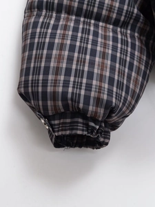 Close-up of elastic cuffs on a plaid padded jacket with silver metal button detail