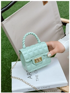 Detail of mint green PVC jelly bag featuring a gold clasp and woven handle outdoors