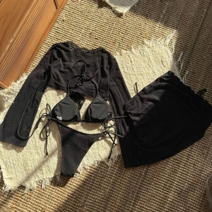 Dettaglio flat lay del set bikini a 4 pezzi nero all'uncinetto con top in rete e gonna
