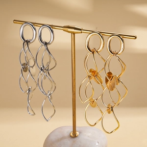 Layered wavy gold and silver hoop earrings hanging on a minimalist metal display stand