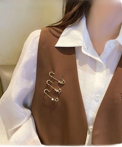 Detailed view of three gold pins with star, heart, and circle charms on a brown vest