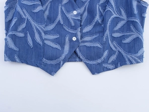 Detailed shot of blue denim vest featuring leaf-shaped fringe textures and white buttons