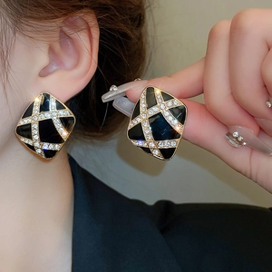Macro shot of geometric black enamel earrings with crossed diamond patterns in gold