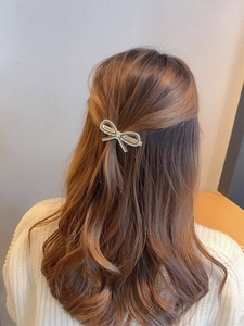 Golden bow hair clip with rhinestones worn on curly brown hair for a stylish look