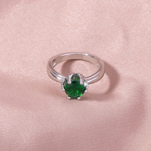 Detailed macro shot of silver ring with green round gemstone on pink silk fabric background