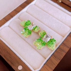 Detailed close-up of green crystal and gold-plated floral earrings on white velvet